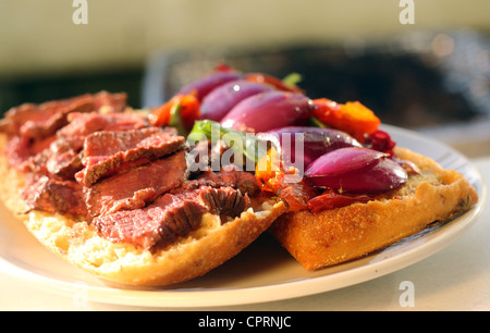 Un barbequed steak sandwich riempito con verdure colorate seduto sulla parte superiore di una piastra bianca sotto il sole. Foto Stock