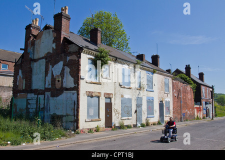 Un uomo su una mobilità unità scooter passato una fila di scorrere verso il basso e abbandonate case abbandonate in Sheffield South Yorkshire, Inghilterra Foto Stock