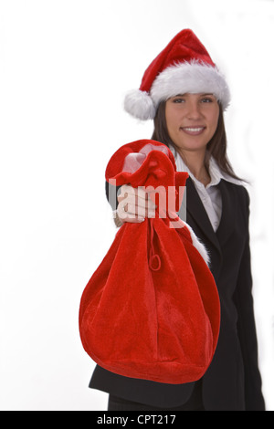 Giovane imprenditrice indossando una santa del cappello e offrendo un sacco rosso pieno di doni.La messa a fuoco è selettiva sul sacco. Foto Stock