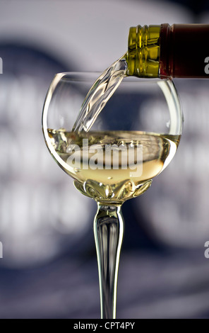 Vino versato, un bicchiere di vino bianco dell'Alsazia in un tradizionale bicchiere decorato a gambo lungo Riesling con botti di vino alle spalle Foto Stock