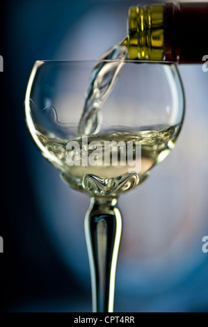 Versando un bicchiere di vino bianco nel tradizionale ornati con gambo lungo deco di vetro con una botte di vino dietro Foto Stock