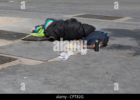 Una persona senza dimora di dormire sulla strada. Una lattina vuota di birra si siede accanto a lui e un paio di monete di piccolo taglio sono sparse intorno. Foto Stock