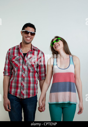 Coppia giovane indossando occhiali da sole e ridere, studio shot Foto Stock