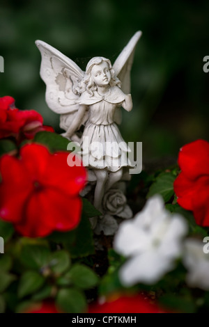 Un piccolo angelo di pietra o di figurine di fata con ali tra fiori rossi e bianchi. Foto Stock