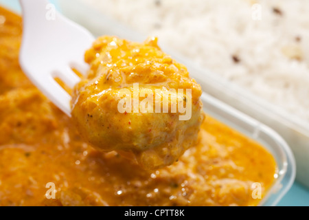 La funzione di sollevamento forche pezzo di Indian take away pasto di pollo o bhoona bhuna curry indiano con riso pilaf su sfondo blu. Foto Stock