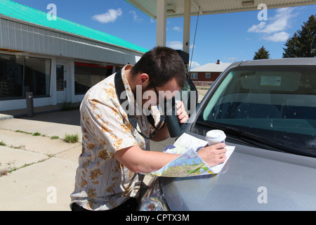 Uomo roadmap di studi con il binocolo con abbandonata la stazione di servizio in background Foto Stock