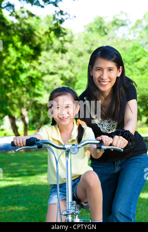 Asian madre figlia di insegnamento per un giro in bicicletta Foto Stock