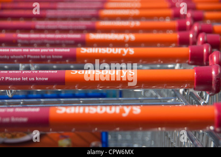 Fila di Sainsbury's shopping carrelli con il carattere distintivo del marchio di colore arancione e maniglie in attesa di utilizzo da parte dei clienti Cardiff Wales UK Foto Stock