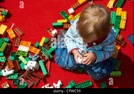 Little Baby bambino ragazza che gioca con la costruzione di blocchi sul tappeto rosso Foto Stock