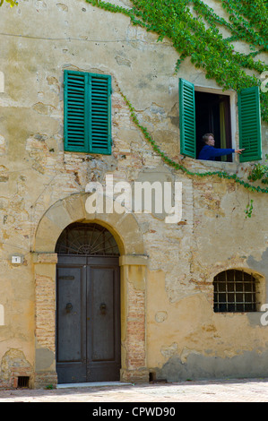 La donna si apre di persiane alle finestre di casa in città sulla collina di Monticcheillo, Val d'Orcia area della Toscana, Italia Foto Stock