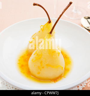 Due pere in una ciotola bianco, affogò in arancione e il succo di limone, guarnita con scaglie di scorza. Foto Stock