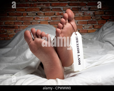 Divertente immagine di un uomo che è in appoggio ricoperta con un foglio come nella morgue, con un'etichetta sul suo pollice. Foto Stock