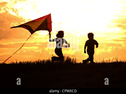 Due bambini volare un aquilone al tramonto richiamare ricordi di infanzia. Foto Stock