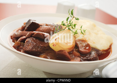 Brasato di manzo con funghi e cipolla cotta nel vino rosso e servito in una tazza di purea di patate. Foto Stock