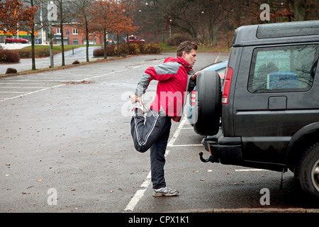 Uomo maturo stretching contro auto nel parcheggio auto Foto Stock