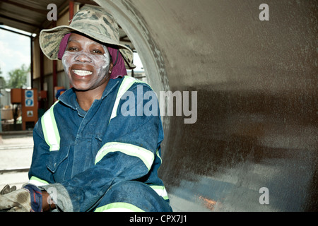 Femmina nero operaio di fabbrica pulisce la parte interna di un tubo di grandi dimensioni, sorridente Foto Stock