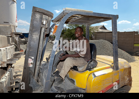 African lavoratore edile aziona un carrello elevatore a forche in un cantiere in costruzione Foto Stock