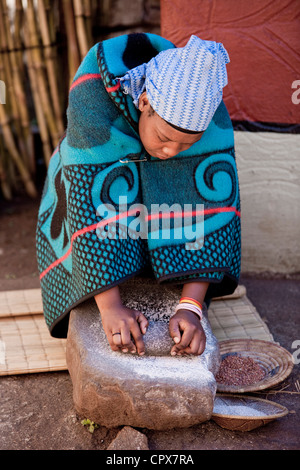 Un tradizionale donna africana macina grano su una roccia Foto Stock