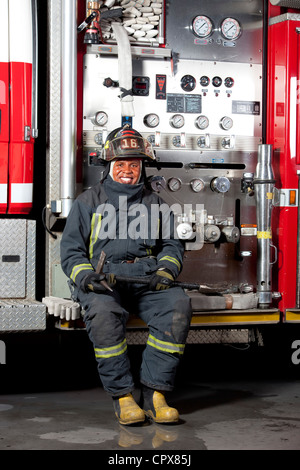 Un vigile del fuoco di seduta sul motore fire, sorridente Foto Stock