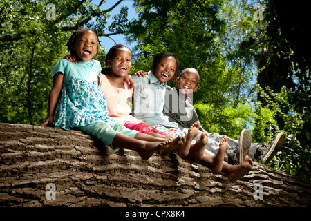 Quattro bambini seduti su un log in un parco Foto Stock