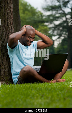 Giovane africano uomo seduto in un parco, al lavoro su un notebook Foto Stock