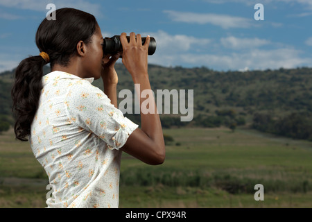 Una donna africana ricerche per gli animali in una riserva di caccia attraverso il binocolo Foto Stock