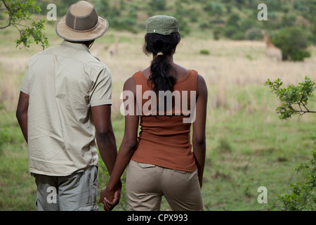 Un africano giovane tenendo le mani durante la visione di una giraffa in una riserva di caccia Foto Stock