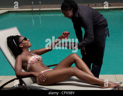 Giovane nero donna sdraiata su una sedia a sdraio accanto a un pool di essere servito Foto Stock