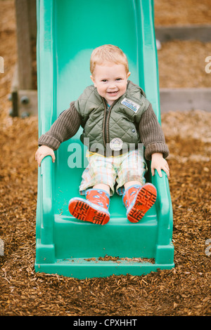 Ragazzo sorridente gioca all'aperto nel parco giochi sulla diapositiva Foto Stock