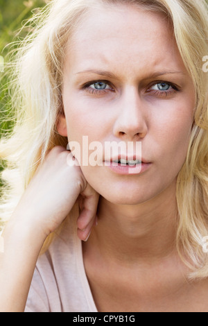 Bella ragazza bionda parlando e guardando la telecamera. Estate ritratto all'aperto contro un sfocato sfondo verde. Foto Stock