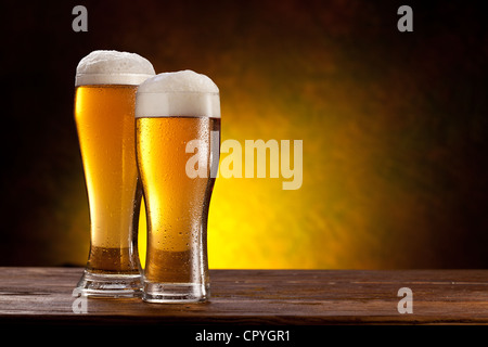 Due bicchieri di birra su di un tavolo di legno. Di colore giallo scuro dello sfondo. Foto Stock