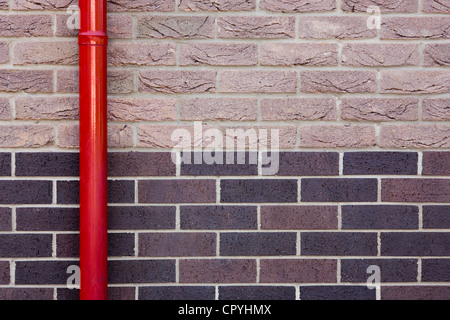 Un rosso drainpipe contro un due toni di un muro di mattoni. Foto Stock