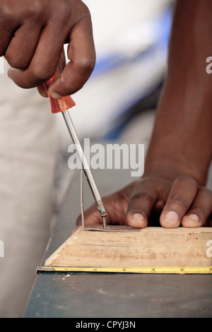 Primo piano di un Africano mans mani avvitando una vite in un pezzo di legno Foto Stock