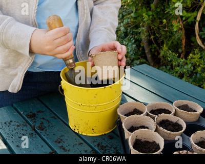 Bambino riempimento di piccoli vasi per piante con il compost per piantare i semi con un cucchiaio e cazzuola. Foto Stock