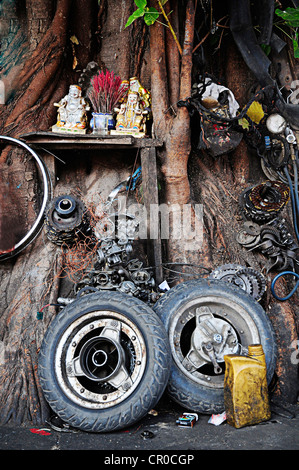 Altare buddista circondato da pezzi di ricambio di un motociclo repair shop in Phnom Penh Cambogia, sud-est asiatico Foto Stock