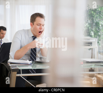 Imprenditore caucasico a bere caffè e sbadigli Foto Stock