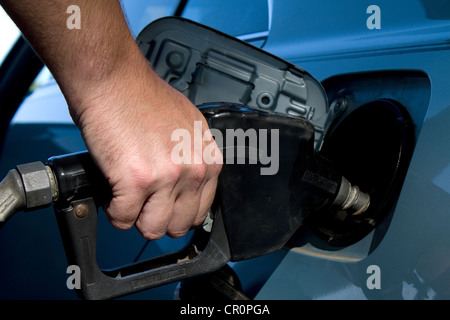 Close up man mano che trattiene il gas maniglia di pompa e il riempimento del serbatoio del carburante sul suo veicolo. Foto Stock