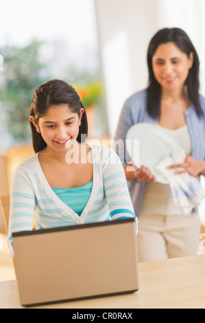 Stati Uniti d'America, New Jersey, Jersey City, ragazza utilizzando laptop (12-13) in casa madre in background Foto Stock