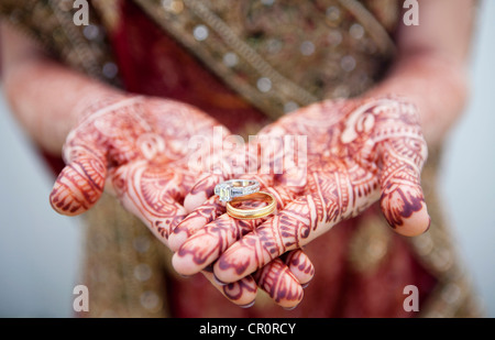 La donna caucasica con Indian Henna Tattoos sulle sue mani tenendo gli anelli di nozze Foto Stock