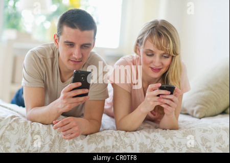 Stati Uniti d'America, New Jersey, Jersey City, giovane sdraiato sul letto e con l'utilizzo di telefoni smart Foto Stock