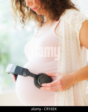 Stati Uniti d'America, New Jersey, Jersey City, ritratto di donna incinta partecipazione delle cuffie sul suo ventre Foto Stock