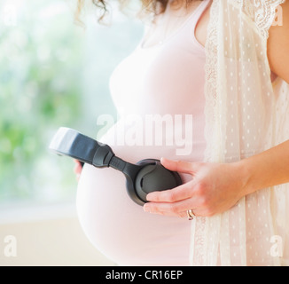 Stati Uniti d'America, New Jersey, Jersey City, ritratto di donna incinta partecipazione delle cuffie sul suo ventre Foto Stock