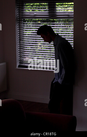 Silhouette di un giovane maschio appoggiata ad una parete per mezzo di una finestra. Foto Stock