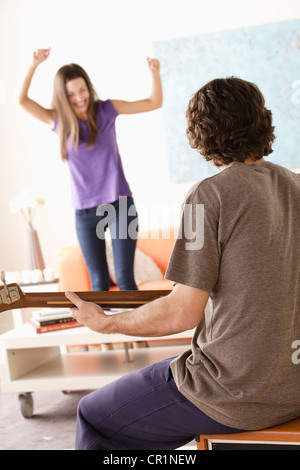 Stati Uniti, California, Los Angeles, giovane di suonare una chitarra elettrica, una giovane donna dancing in background Foto Stock