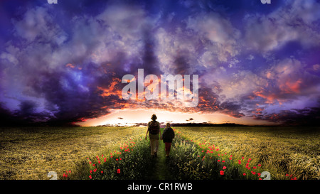 Donna e bambino a camminare su una strada fiancheggiata da fiori di papavero attraverso il centro di un campo di mais, il tramonto con un cielo nuvoloso Foto Stock