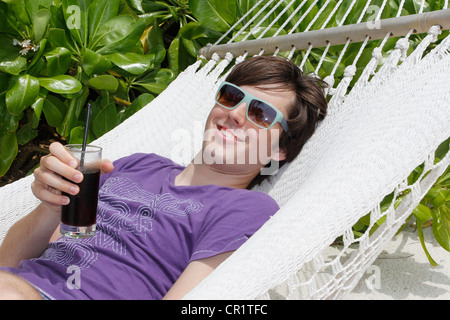 Giovane uomo per rilassarsi in un'amaca, tenendo in mano un drink, Maldive, Oceano Indiano Foto Stock