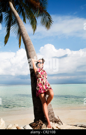 Spensierato giovane donna rilassante con il suo ritorno a un albero di palma su una sabbiosa spiaggia tropicale mentre godendo una vacanza isola Foto Stock
