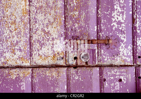 Sullo sfondo di un vecchio dipinto, sbriciolato porta. Maniglia viola su tavole di legno. Foto Stock