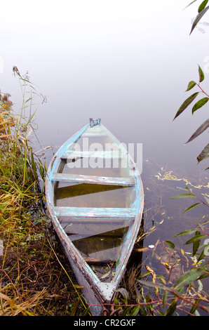 Affondata la barca di legno riempita con acqua stand su foggy river coast shore. Trasporto romantico. Foto Stock