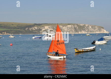 Un marinaio guida il suo dinghy in baia a Swanage, Dorset. Chalk scogliere di Ballard Down sono in background. Foto Stock